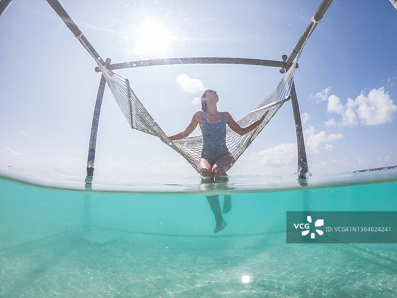 一名女子在热带泻湖上的吊床上放松，水下有屏风图片素材