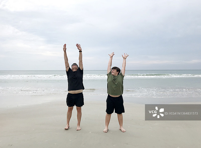 爸爸和他的儿子在海滩上做伸展运动和瑜伽的尴尬和有趣的肖像图片素材
