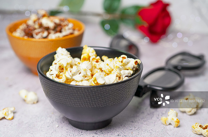 在碗里放上一份爆米花，旁边放上3D电影眼镜和红玫瑰，在情人节晚上一起看电影图片素材