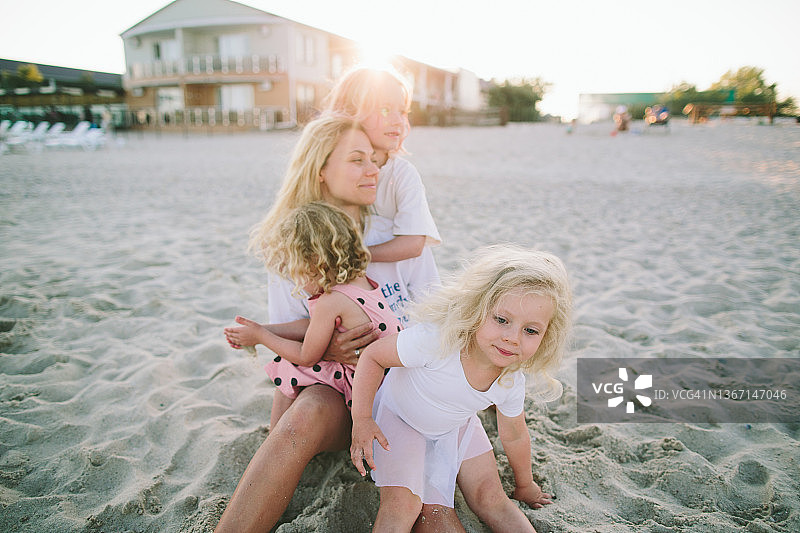 年轻的金发女人母亲和她的3个女儿在酒店的沙滩上玩在一个夏天的日落图片素材