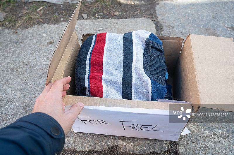 有人拿着一箱衣服在街上捐赠，却把它扔在地上。图片素材