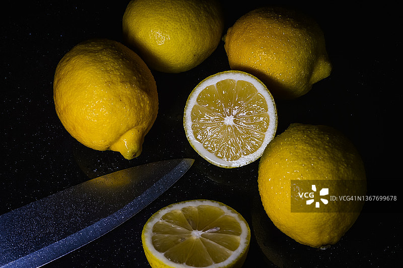 在闪亮的黑色玻璃背景上，用刀片将半个柠檬和整个有机柠檬排列在一起图片素材