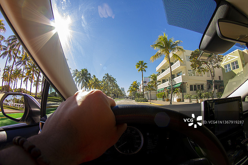 视角拍摄的一个年轻的运动男子驾驶汽车在迈阿密海滩地区的天堂蓝色的海洋景观，迈阿密，南佛罗里达，美国-美国图片素材