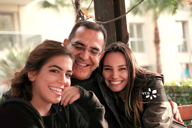户外的父亲和两个年轻的女儿坐在公园的长椅上图片素材