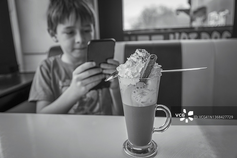 拿着智能手机的男孩在餐厅享受奶昔图片素材