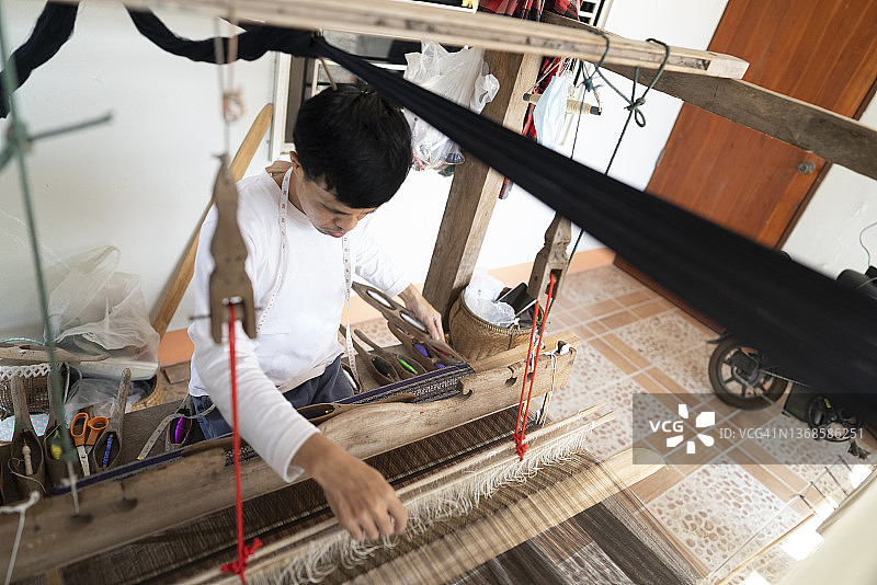 年轻的亚洲男子用传统的木制织布机编织本土布料。日常生活中的可持续性图片素材