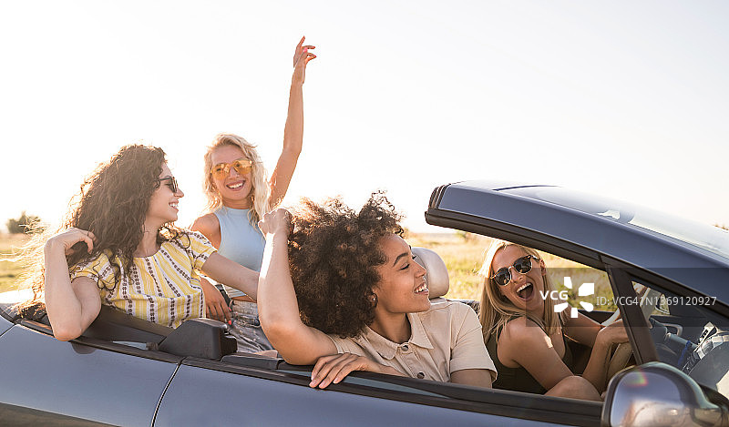 多种族的兴奋的年轻女性享受汽车乘坐敞篷车在日落图片素材