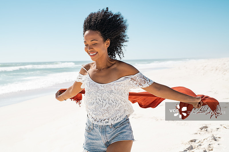 无忧无虑的黑人妇女戴着围巾在沙滩上奔跑图片素材