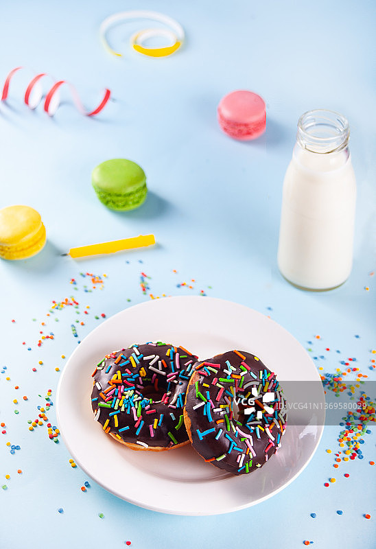 美味的甜甜圈配上巧克力糖衣和生日蜡烛，背景是牛奶和马卡龙。图片素材