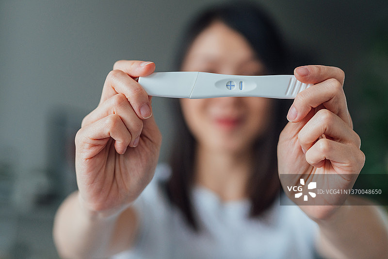 快乐的年轻亚洲妇女拿着家里的怀孕测试试剂盒图片素材