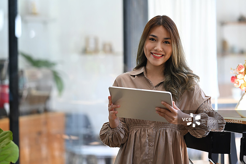吸引人的亚洲女企业家，拿着数码平板电脑，对着相机微笑。图片素材