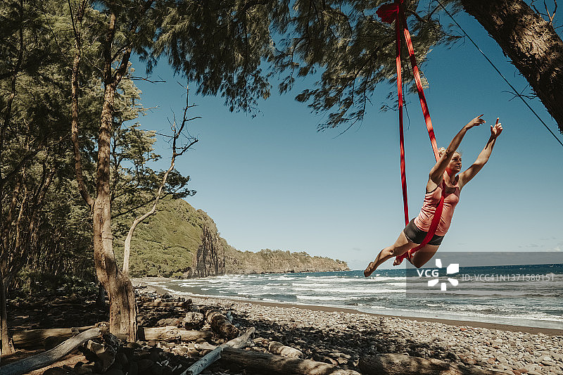 一名女子在夏威夷热带海滩上的空中丝绸吊床上表演图片素材