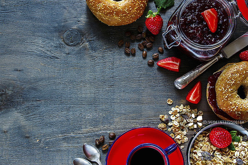 俯瞰咖啡杯，格兰诺拉麦片，新鲜的百吉饼与果酱和草莓早餐在质朴的木制背景图片素材