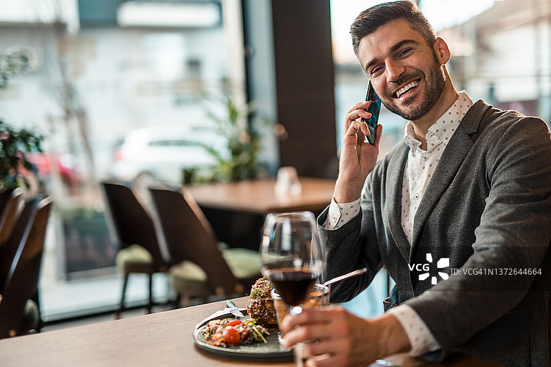 一个快乐的年轻人在餐馆吃午饭，一边打电话。图片素材