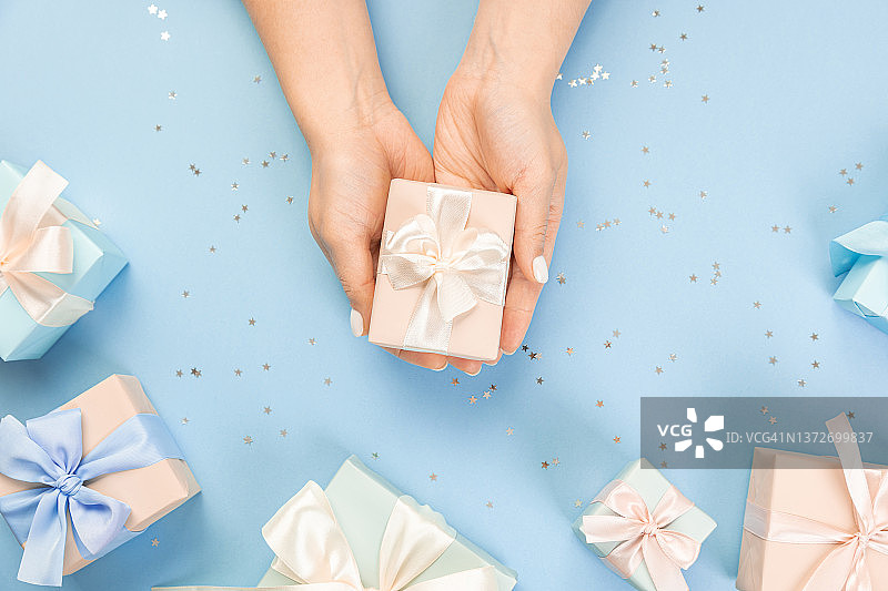 女人的手平躺着一个礼物包装和装饰在蓝色背景与银色亮片与副本空间的桌子的一部分被几个节日包装的礼物包围图片素材