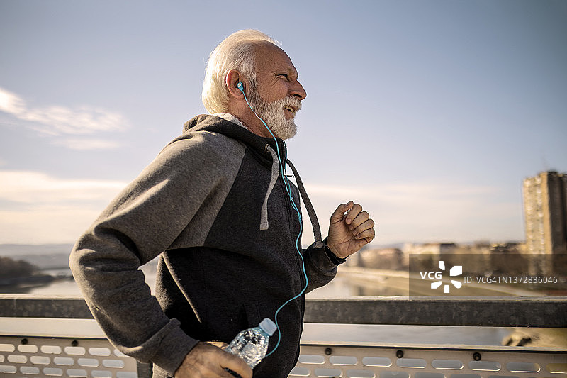 老年人戴着耳机在城里慢跑图片素材