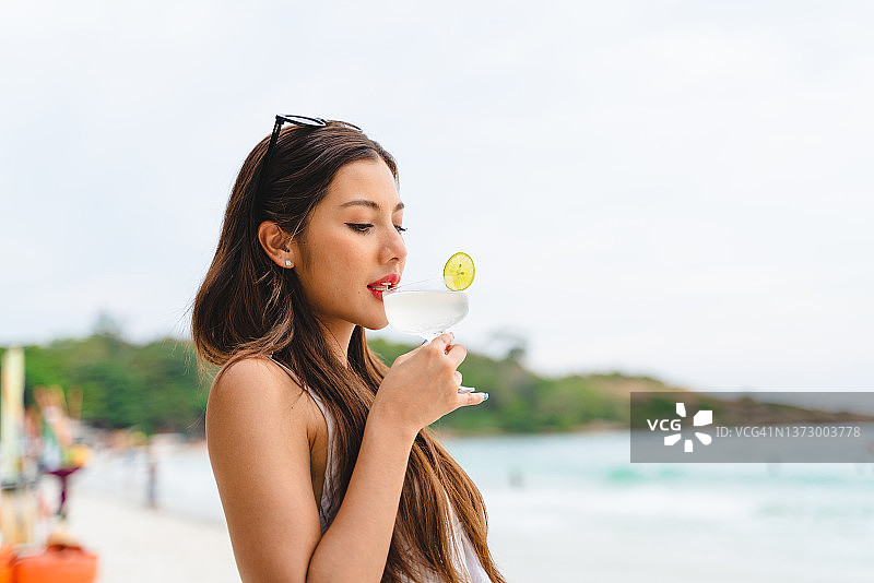 美丽的亚洲女人在海滩上喝鸡尾酒图片素材