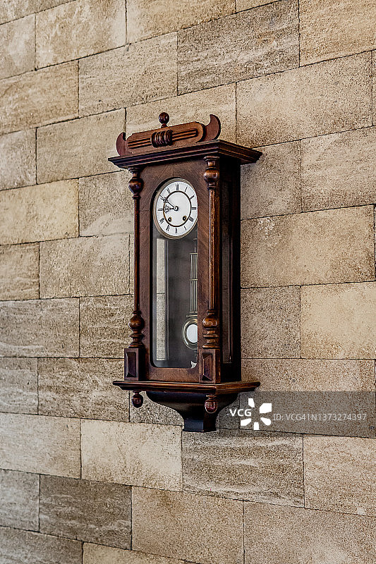 墙上的老式木钟，墙上有一个钟摆。机械表与罗马数字在表盘上。光背景。图片素材