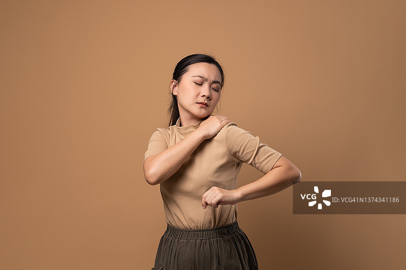 一名亚洲妇女因身体疼痛而孤独地站在米色背景上。图片素材