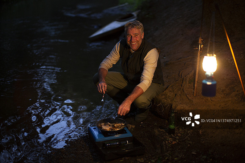 肖像快乐的人在夜间在河边用野营炉做饭图片素材