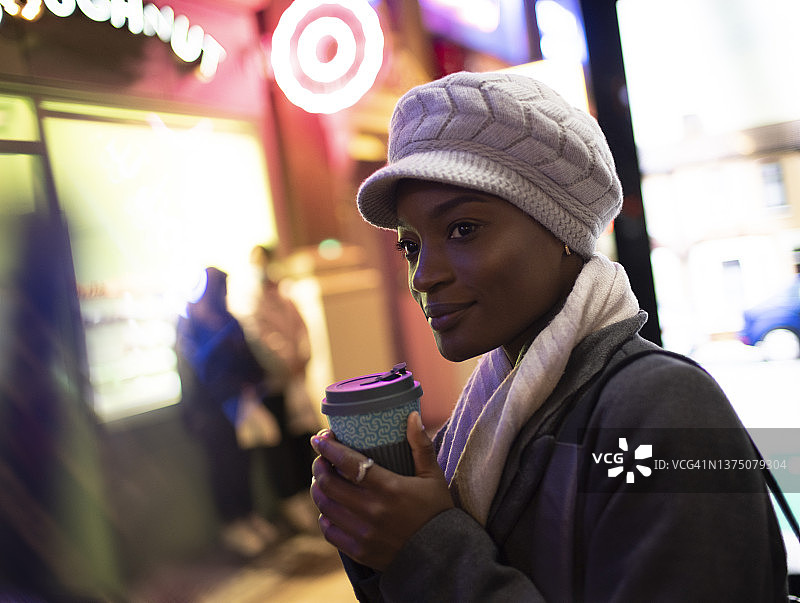 时尚的年轻女子戴着帽子在城市的人行道上喝咖啡图片素材