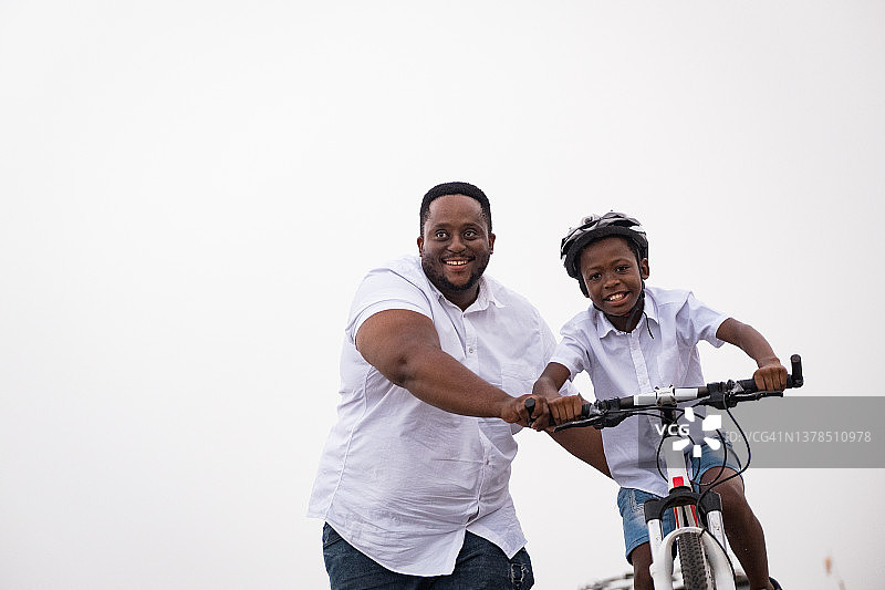 父亲帮助儿子骑他的新自行车。图片素材