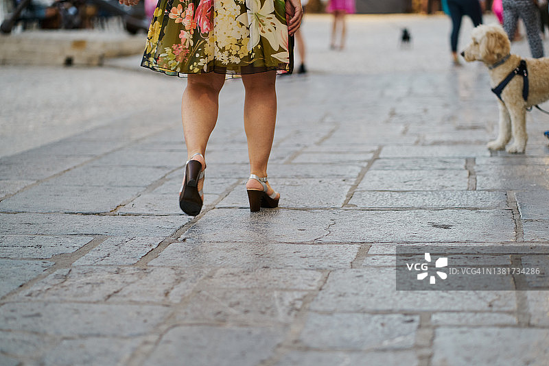 一个穿着连衣裙和高跟鞋的女人在一条小路上走着。图片素材