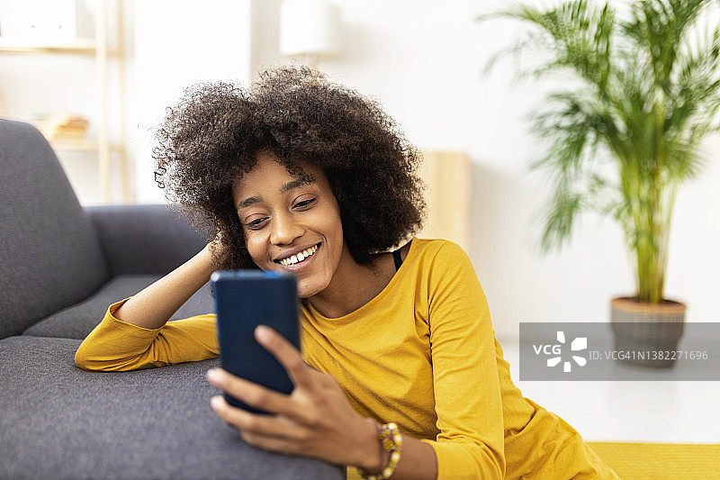 微笑的女人靠在家里的沙发上使用智能手机图片素材