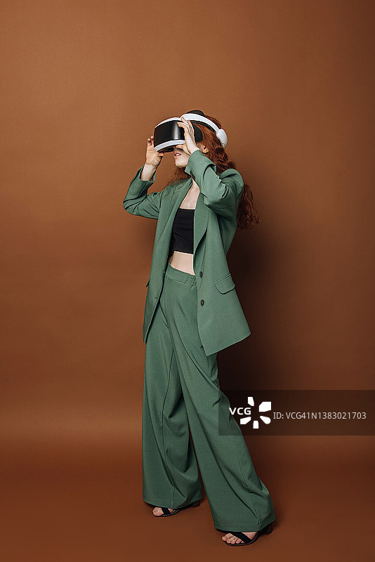 美丽的年轻白人女子在一个相信现实的头盔玩游戏。戴着虚拟现实眼镜的女士在彩色背景上使用科技。图片素材