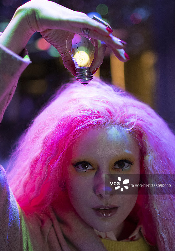 肖像酷女人与粉红色的头发持有灯泡在头上图片素材