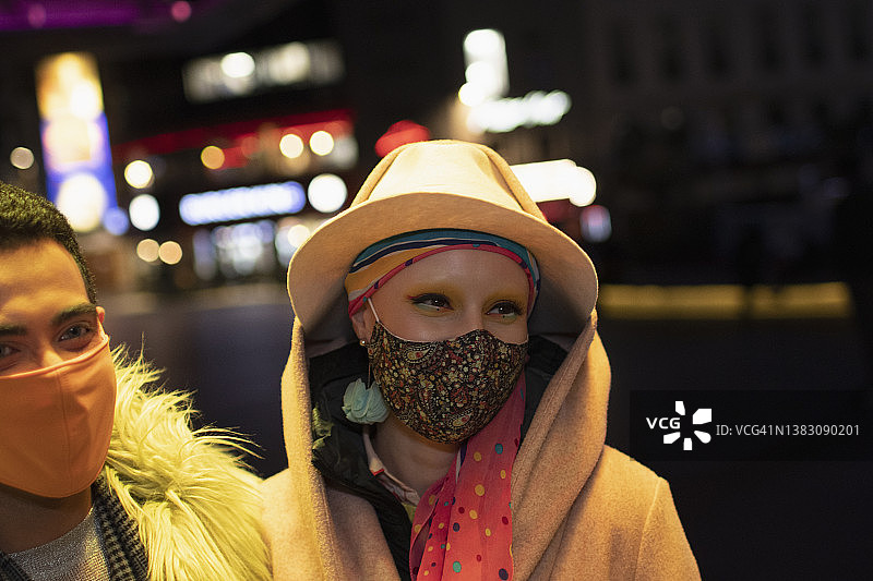 戴着面具的快乐时尚夫妇晚上在城市街道上图片素材
