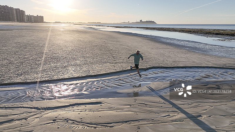 鸟瞰图，男子奔跑在空旷的海滩上图片素材