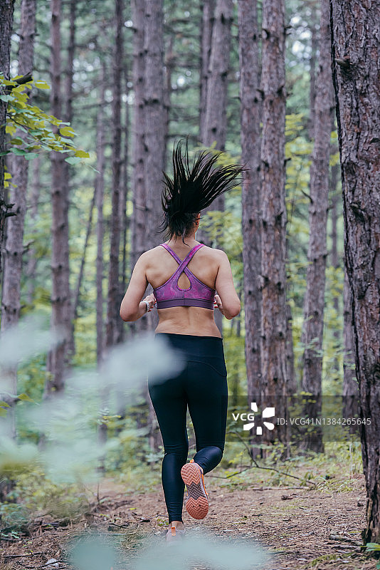 这是一名年轻的运动女性在森林中奔跑的背影图片素材