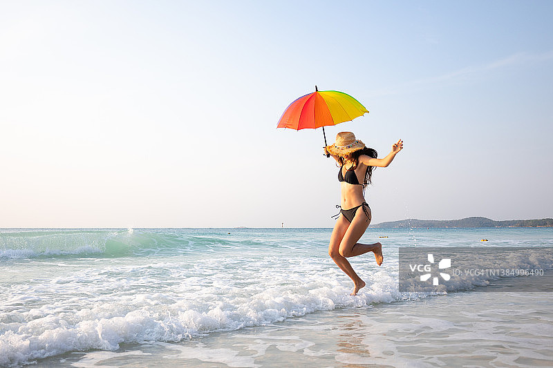 性感快乐的女人在白色的沙滩上自由地跳着，戴着太阳帽。图片素材