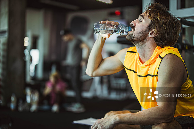 一名口渴的男子在体育馆里休息时喝水。图片素材