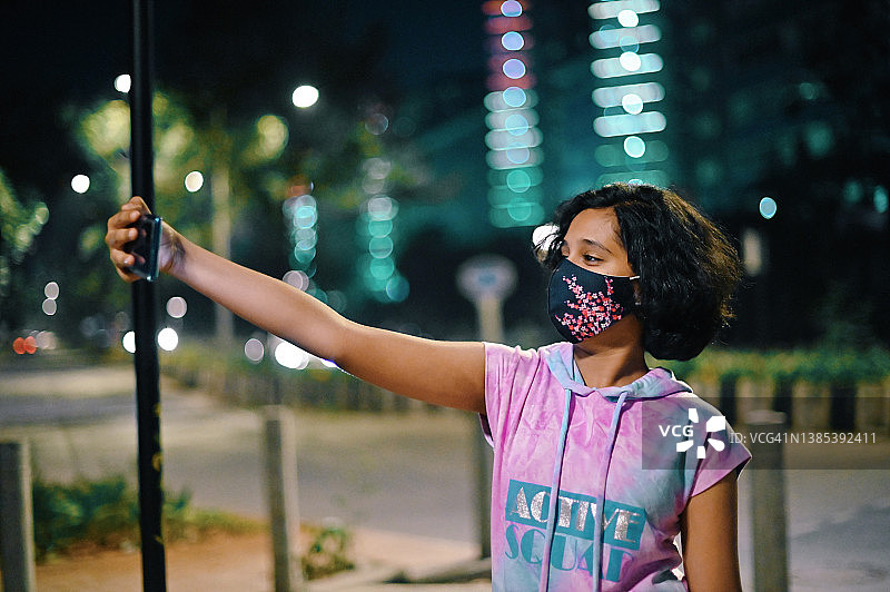 一个十几岁的女孩晚上站在城市的街道上玩手机图片素材