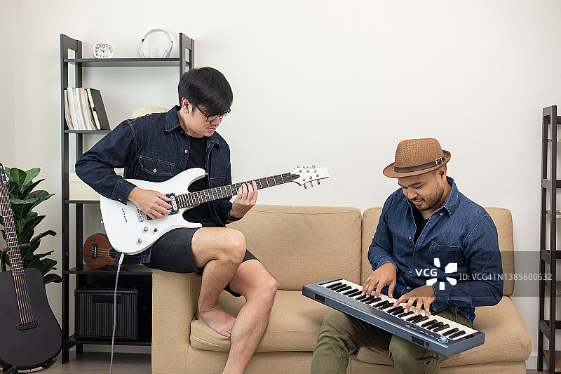 生活方式的概念。这个周末，年轻的亚洲音乐家和朋友在家里的客厅里玩电吉他。用歌曲和音乐放松自己。亚洲人玩摇滚吉他很开心图片素材