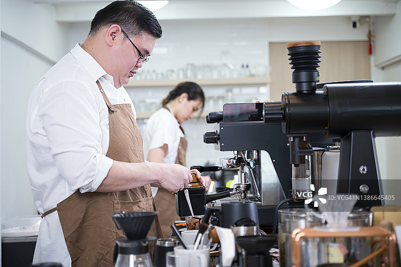 侧视图的男性和女性咖啡师在咖啡馆为顾客煮咖啡。咖啡厅、小企业、销售点和外卖。图片素材