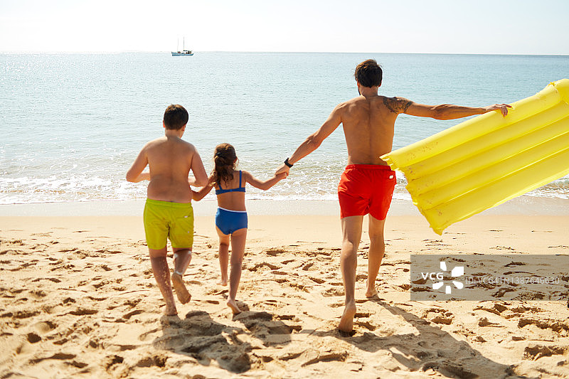 一位父亲带着他的两个孩子在海滩度假。图片素材