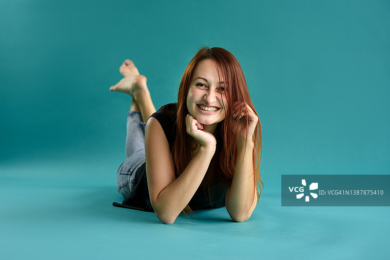 近距离的快乐的红发年轻女子微笑的脸躺在蓝色的背景。本空间图片素材