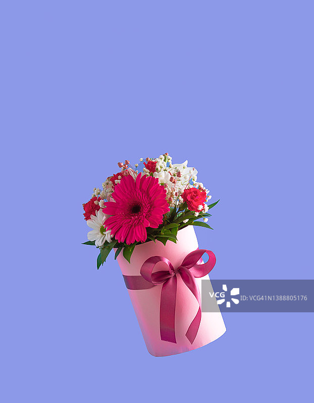 粉红色的礼盒，紫色的背景上点缀着各种春天的花朵。母亲节的想法。副本的空间。图片素材