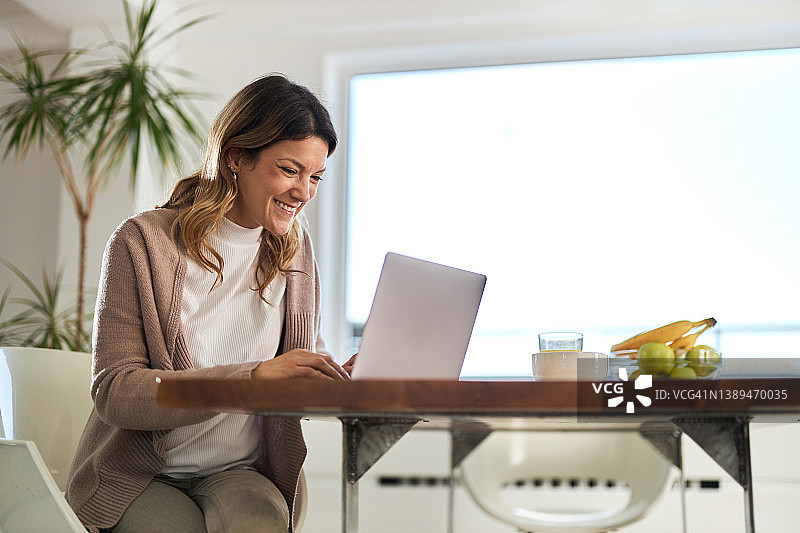 快乐的女商人在家庭办公室用笔记本电脑工作。图片素材