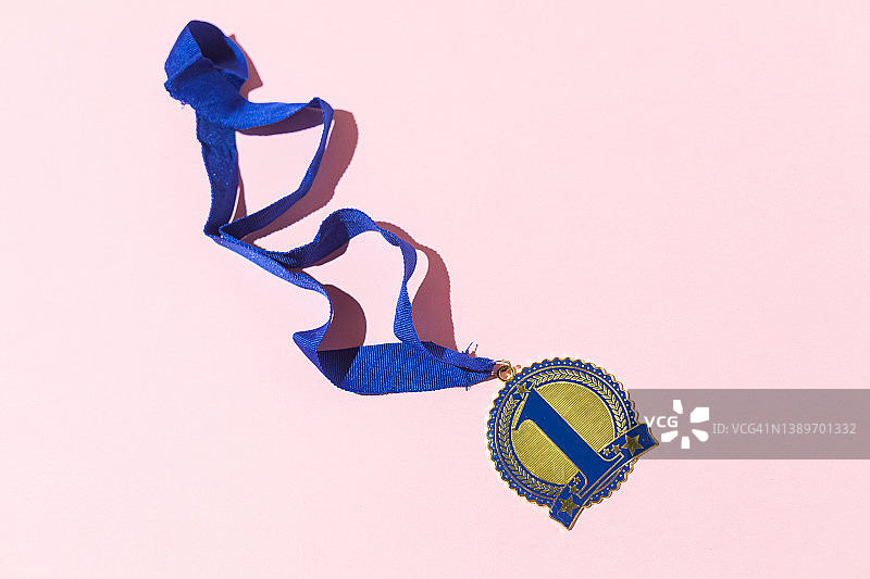 第一名冠军奖牌与数字1蓝色和蓝色带子在粉红色的背景。竞争的概念，优胜者，运动，胜利，冠军和第一名。图片素材