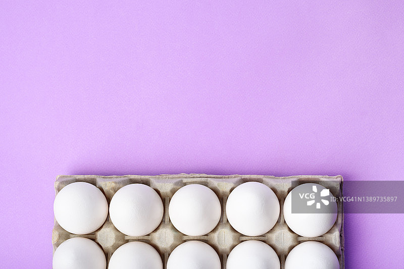 许多白色鸡蛋在工艺纸盒上紫色的背景。复活节假期的概念。图片素材