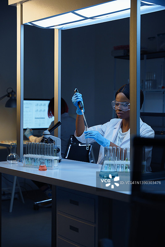 美丽的非裔美国医生在工作，坐在现代实验室的办公桌前，在试管里搅拌液体图片素材
