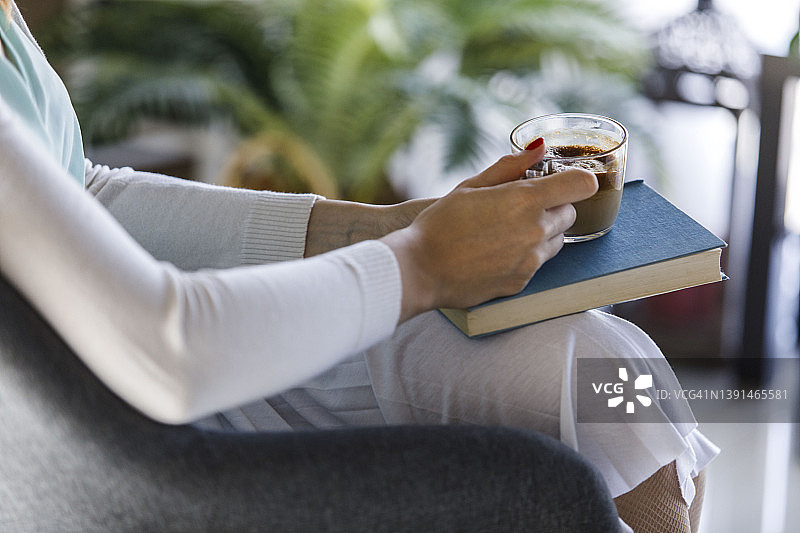 一个陌生女人的腹部，拿着一杯咖啡放在她读完的书上图片素材