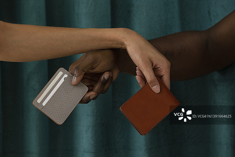一名黑人男子和西班牙裔女子的手都拿着皮革钱包的特写。图片素材