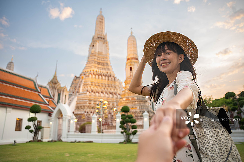 年轻美丽的女人在曼谷寺庙旅行期间握着男朋友的手的后视图。图片素材