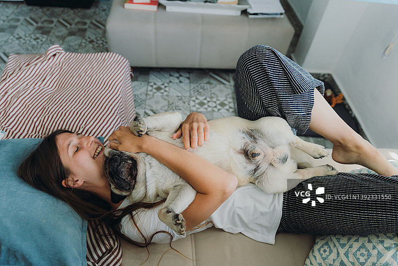 女人躺在沙发上和她的狗狗玩耍图片素材