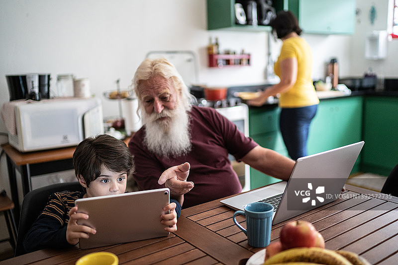 爷爷在家里用笔记本电脑，孙子在家里用平板电脑图片素材